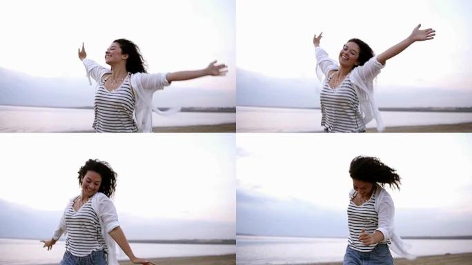 一个美丽的卷发黑发女人的肖像，伸出双手快乐地在海边或湖边奔跑。穿着白色休闲服。微笑，快乐，自由