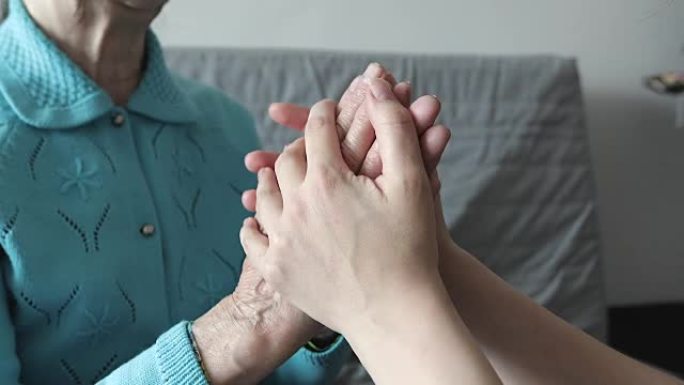 一位年轻女子握着一位老祖母皱巴巴的手。