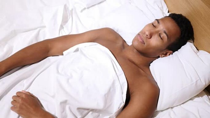 放松的非洲年轻人晚上睡在床上的俯视图