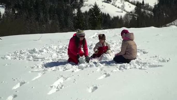 快乐的家庭在冬天在山上的白雪皑皑的森林里玩耍。妈妈和她的两个孩子扔雪球。堆雪人。他们在笑。
