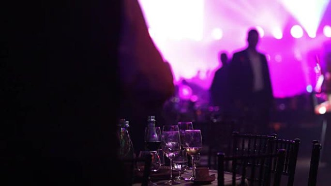 在餐厅或夜总会举行的青年聚会，在跳舞的人的剪影，舞台灯光和紫色填充的背景下摆满酒精和食物的宴会桌