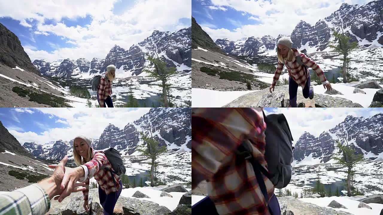 夫妇在加拿大落基山脉的心脏地带徒步旅行，男人伸出手协助山顶上的女性