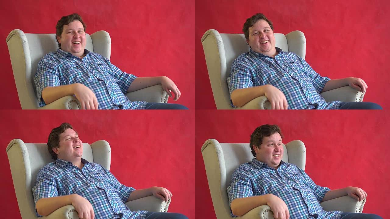年轻的胖子，格子衬衫，坐在椅子上，在红色背景上大声笑孤立-有趣的概念