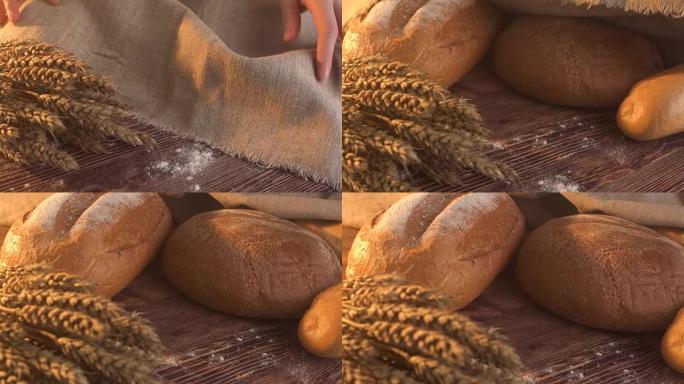 手工制作的美味面包躺在木桌上的粗麻布上，上面有面粉，小麦和麦穗