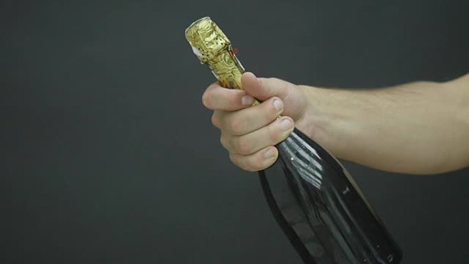 一个男人的手拿着一瓶香槟，背景是黑色的