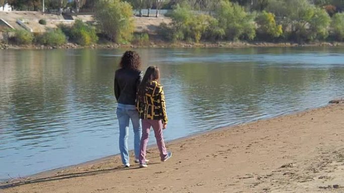 一个女人和一个女孩在河边散步。母女俩沿着河岸散步