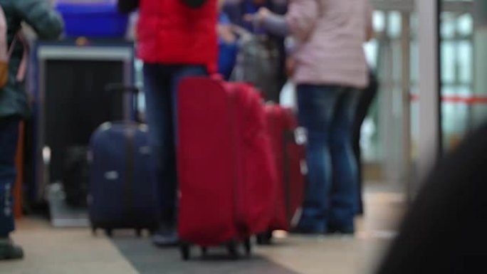 机场安检入口行李控制。扫描行李。一个男孩和一个大的红色行李箱的家庭通过入口控制装置，将行李装载到手推