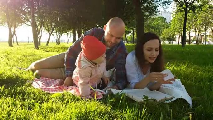 幸福的家庭躺在草地上，在公园日落时与孩子一起野餐时看书