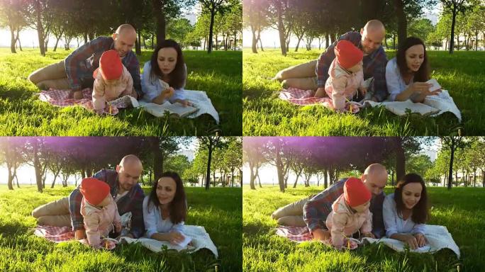 幸福的家庭躺在草地上，在公园日落时与孩子一起野餐时看书
