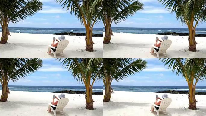 女人在度假时放松，坐在棕榈树下的热带海滩上，坐在躺椅上阅读电子书或电子阅读器