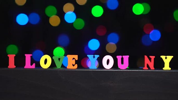 彩色单词 “i love you NY” 来自抽象模糊灯光前的多色木制字母bokeh背景