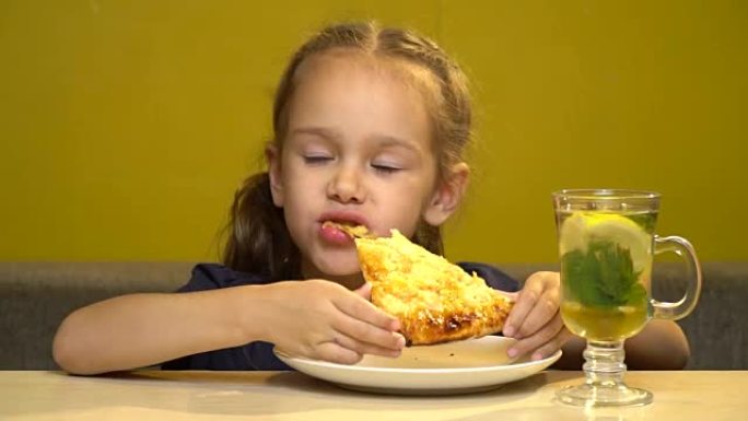 咖啡馆里的小女孩正在用手吃披萨。桌子上是一杯茶和薄荷，蜂蜜和柠檬。