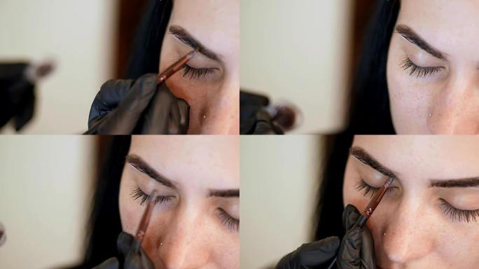 特写。年轻女子接受眉毛矫正手术。kosmetolog-化妆师在美容沙龙用画笔涂在眉毛上。面部专业护理