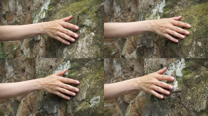 女人在慢动作中靠着旧石墙画手。女性手触摸岩石粗糙表面