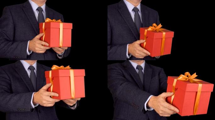 高加索商人拿着并赠送红色礼品盒。从不聚焦到聚焦运动。穿着经典西装的成年男子拿着红色礼品盒。阿尔法通道