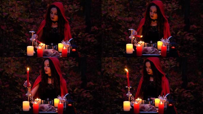 迷人的美丽黑发女巫，穿着红色斗篷的书，在神秘的秋天森林中让人联想到。带有心脏，鸡腿和豪猪针的巫术