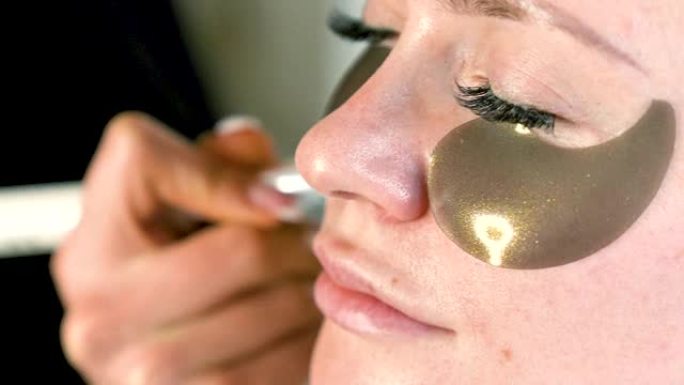 有眼罩的女人脸的特写。化妆师用刷子在脸上涂抹化妆品色调粉底。