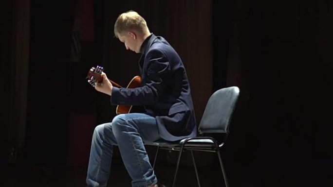男子在聚光灯下在舞台上演奏原声吉他，不插电表演。侧视图