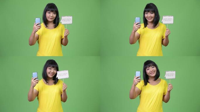 美丽快乐的亚洲女人拿着手机和自拍纸标志