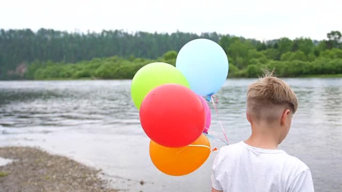 一个少年拿着气球。湖边大自然的暑假。庆祝和乐趣。孩子的生日