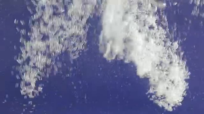蓝色水中的白色气泡流。倒水飞溅并产生湍流气泡