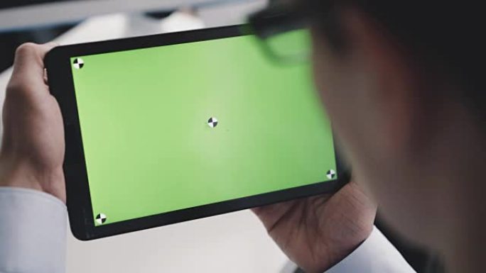 A man reading from a tablet PC with a green screen