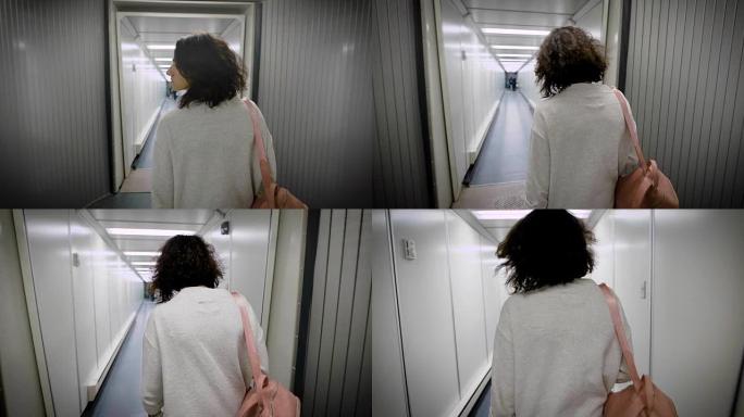 悲伤疲惫的年轻黑发女郎穿着休闲风格，正走在一座轻便的现代喷气桥里，后视图