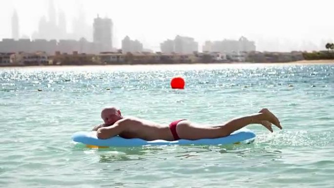 一个人在充气床垫上休息，在海里游泳，晒日光浴。辛苦工作一周后休息商人。在城市摩天大楼的背景下