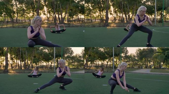 年轻漂亮的女人在公园的足球场上伸展，其他健身模型在背景中锻炼，晨练