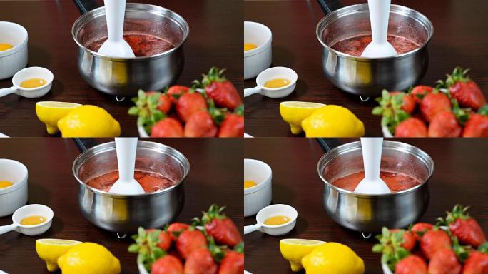 在不锈钢锅中用浸入式搅拌器研磨水果的特写镜头，烹饪酱，果酱，草莓制成。