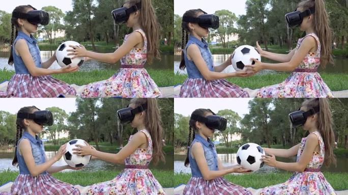 两个孩子玩虚拟游戏。他们坐在河岸草坪上的虚拟现实眼镜中，手里拿着一个足球，扭动着。