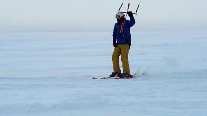 慢动作:一名男运动员正在滑雪板上放风筝。他在一个大湖的冰面上打滚。翻滚时，他会进行各种跳跃、动作和其