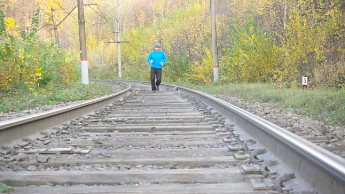 男人慢跑火车轨道铁路在秋天的季节在森林。在鼓舞人心的秋季风景中越野跑步时进行户外训练和锻炼。体育动机