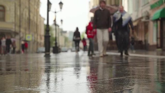 反射剪影在雨中潮湿的沥青池中，在城市街道上的雨天背景。实时。雨中带伞的人上下班。模糊的波克。自然背景