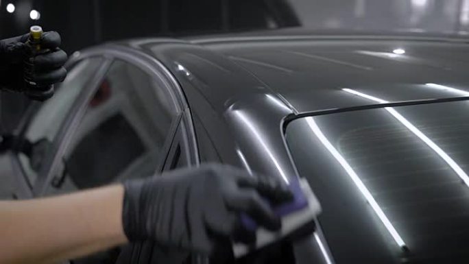 大师正在用海绵用纳米陶瓷液体摩擦汽车表面，手里拿着瓶子，在自动服务中