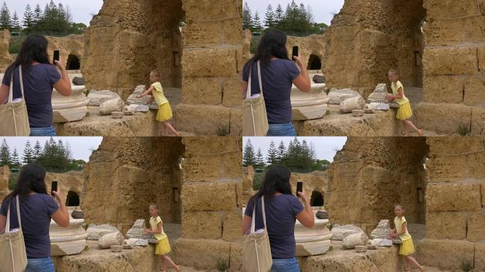 年轻的母亲在废墟的迦太基突尼斯给女儿拍照