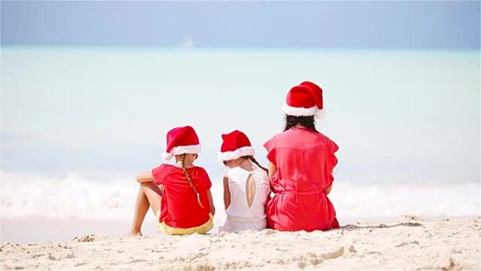 在热带海滩上，戴着红色圣诞老人帽子的幸福美丽的家庭庆祝圣诞节。妈妈和孩子们享受圣诞节假期
