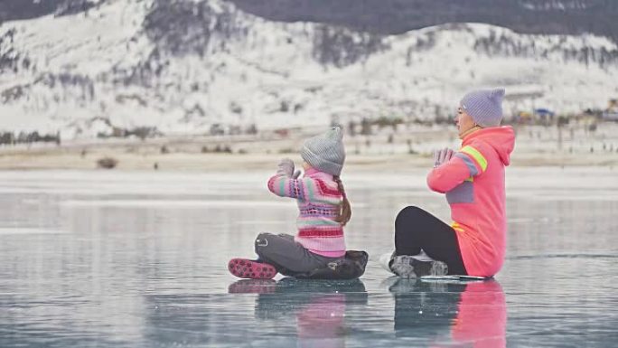 一家人在冬天练瑜伽。女人在大自然的冰上做伸展和冥想。母亲和女儿在裂缝里的冰上练习瑜伽。女孩们在户外做