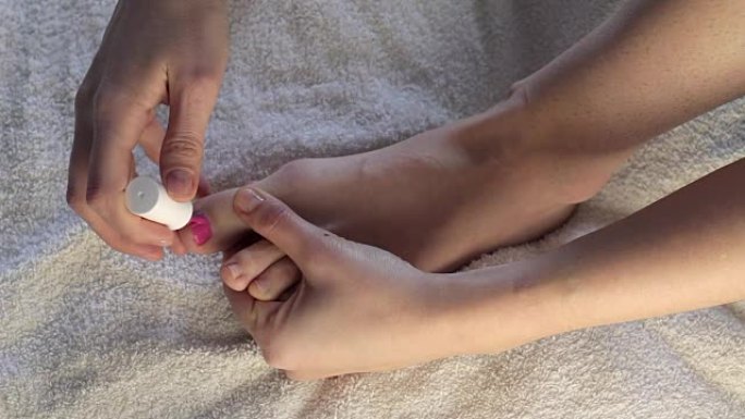 女人的手画脚趾甲。女孩在脚上画指甲粉红漆