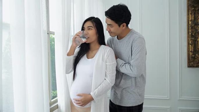 年轻的丈夫用喝水照顾怀孕的妻子