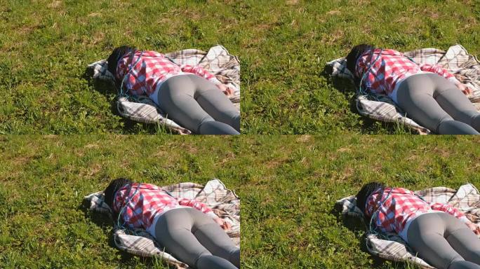 无法辨认的蓝色非洲辫子的女人睡在公园的草坪上。