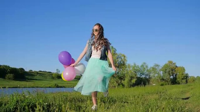 快乐的女孩少年，头发上有彩色的头发，手里拿着气球，在湖附近的绿色草地上玩得开心