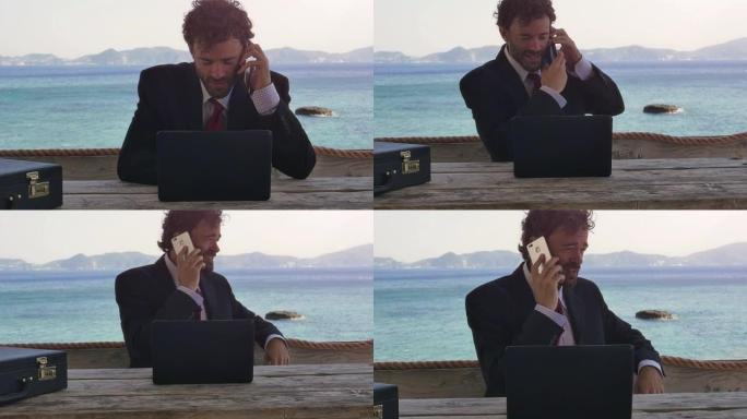 穿着西装的男子在海边的一个岛上的阳台上用智能手机聊天，手提电脑