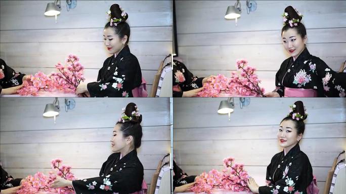 穿着传统日本和服的美丽艺妓坐在餐厅的一张空桌子上，在樱花的树枝上采摘。