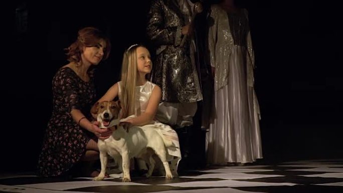 妈妈和女儿在明亮的国王和王后的背景下拍着站在棋盘上的狗。现场象棋比赛。