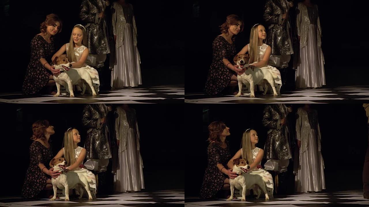 妈妈和女儿在明亮的国王和王后的背景下拍着站在棋盘上的狗。现场象棋比赛。