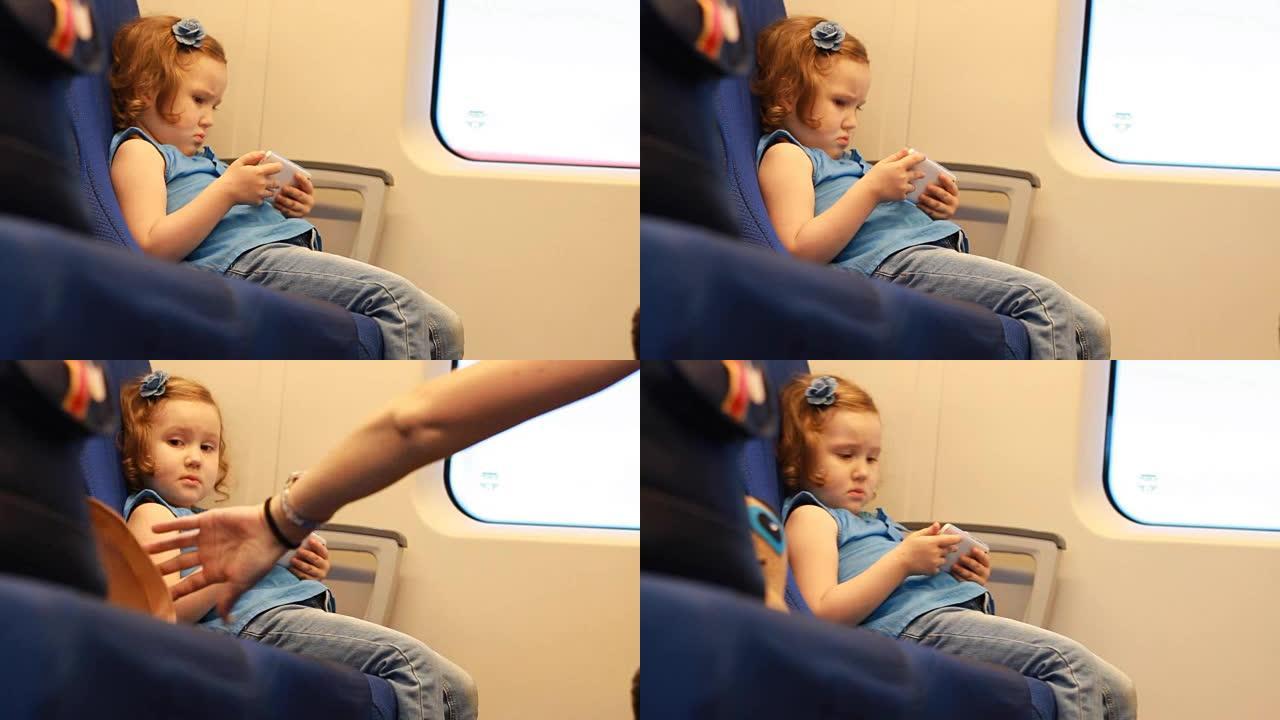 女童在火车上玩智能手机。在快车里玩手机游戏的宝贝。旅行，旅行，道路的概念