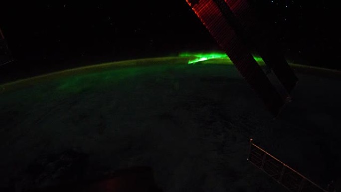 在地球北极上方看到的明亮的绿色极光。前景中可以看到国际空间站的太阳能电池板。剧照由美国宇航局约翰逊航