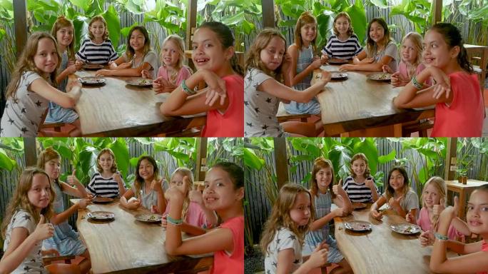 一群多民族的年轻女孩坐在桌子旁竖起大拇指