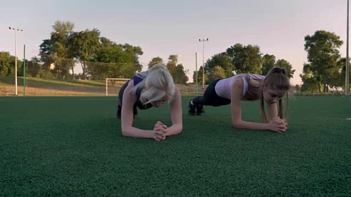 两个年轻漂亮的女人早上在公园的足球场上做木板锻炼，健身模型锻炼